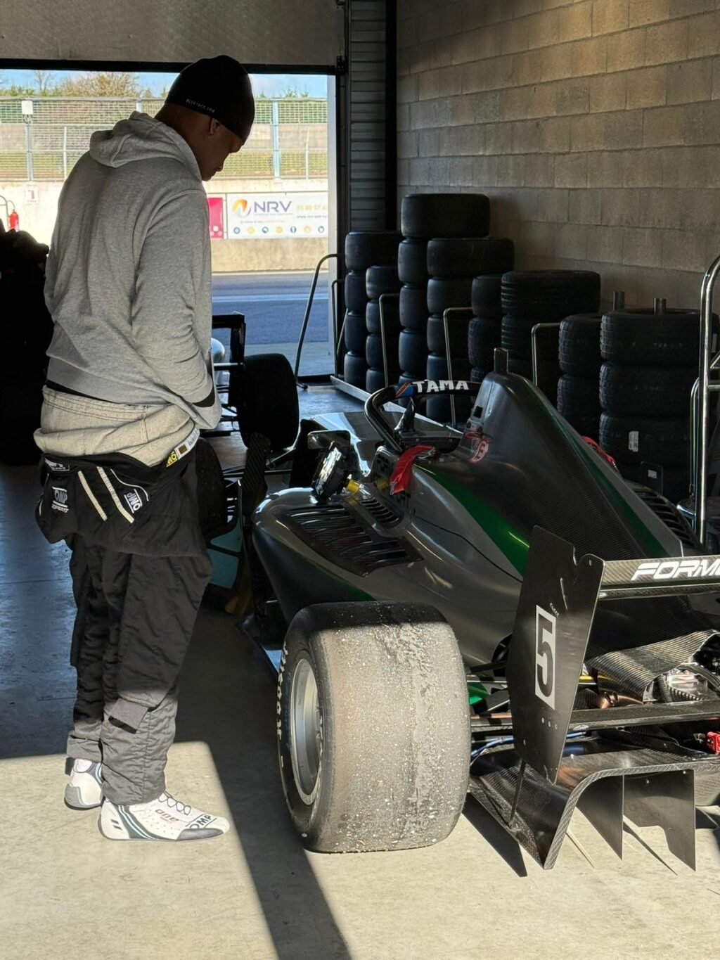 Dans les stands, avant la piste. Tjay Tama inspecte sa Formule 3 — celle qui porte son nom et son rêve